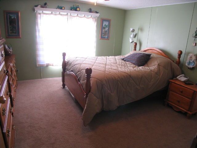 Bedroom with a bed, dresser, and nightstand. Window has curtains and a shelf with toy tractors