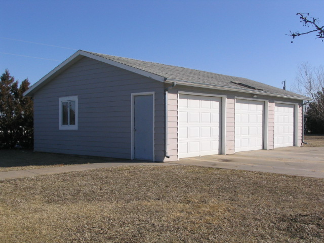 Gray sided garage with three white overhead doors and a single side door