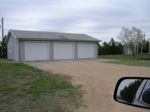 1995 Ford Bronco - A detached garage with three large overhead doors and a single side door sits under a cloudy sky.