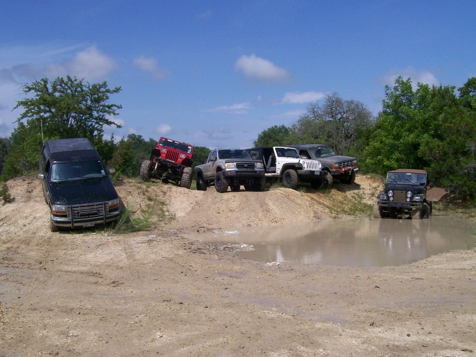 Lineup of lifted 4x4 trucks and Jeeps on a sandy trail by a mud puddle