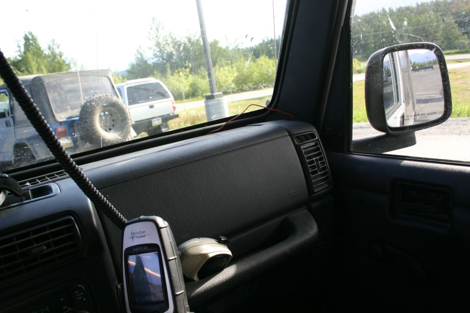 Interior of a Jeep Wrangler showing a handheld GPS device and two other vehicles outside