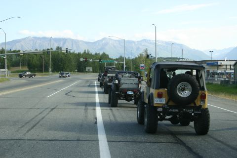 2003 Jeep TJ - A convoy of Jeep Wranglers drives down a highway with mountains in the background.