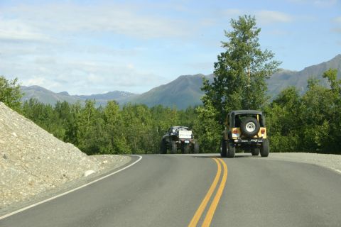 2003 Jeep TJ - Two off-road vehicles travel down a scenic highway surrounded by trees and mountains.