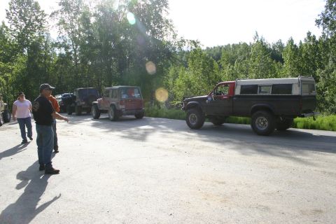 2003 Jeep TJ - Multiple off-road vehicles are lined up on a paved area with a wooded area behind them.