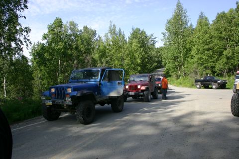 2003 Jeep TJ - Several Jeeps and a black pickup truck are parked on a dirt road lined with trees.
