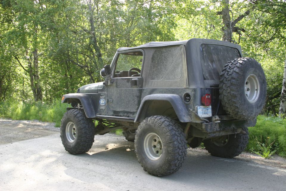 Dark green Jeep Wrangler with soft top, seen from rear-three-quarter view on a dirt road