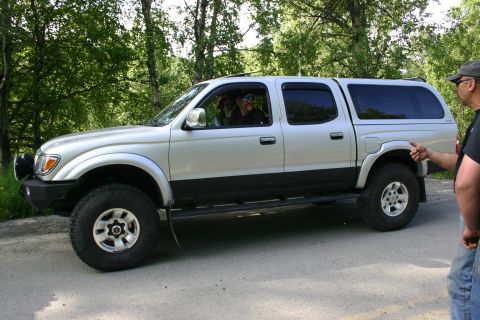 2003 Jeep TJ - Silver Toyota Tacoma pickup truck with a camper shell and aftermarket wheels is parked on a dirt road.