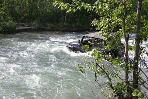 2003 Jeep TJ - A Jeep Wrangler navigates a turbulent river, surrounded by lush green foliage.