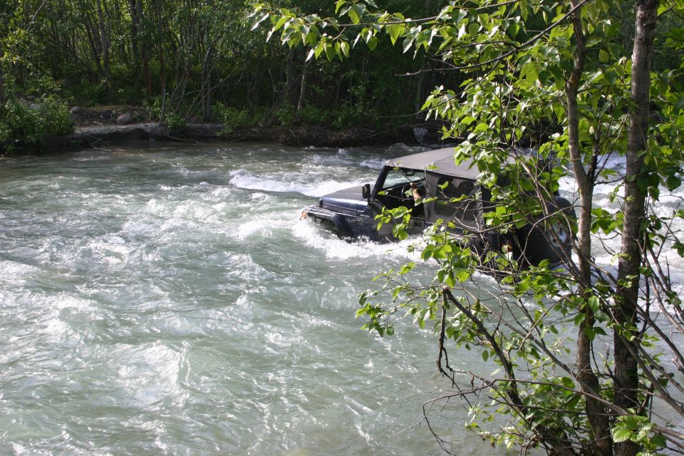 Black Jeep Wrangler driving through a fast-moving river with trees on the bank