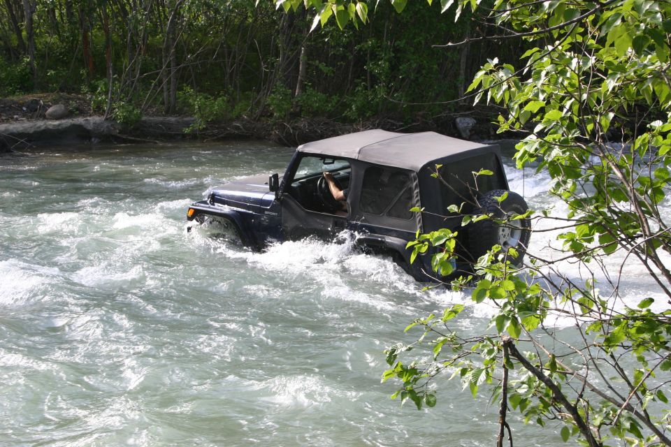 Black Jeep Wrangler TJ driving through a river, soft top up, spare tire on rear