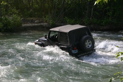 2003 Jeep TJ - A black Jeep Wrangler navigates through a fast-flowing river, with a website address visible on the rear bumper.
