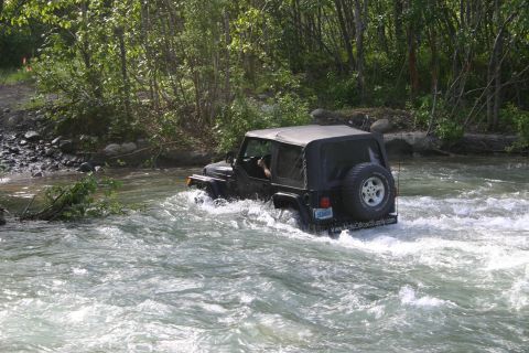 2003 Jeep TJ - Jeep TJ navigating a river with trees and rocks on the bank.