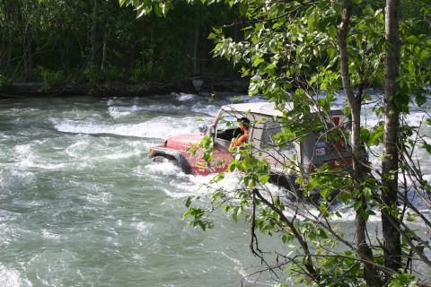 2003 Jeep TJ - A red Jeep Wrangler navigates a fast-flowing river surrounded by trees.