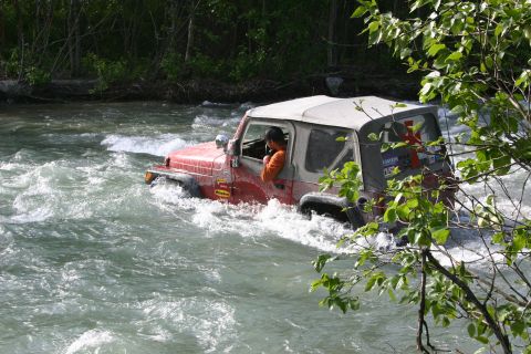2003 Jeep TJ - A red 2003 Jeep TJ navigates through a fast-flowing river, demonstrating its off-road capabilities.