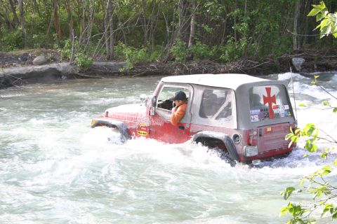 2003 Jeep TJ - A red 2003 Jeep TJ navigates a river, kicking up white water.