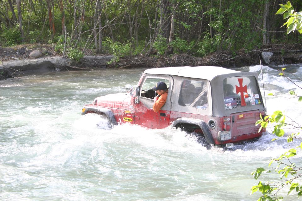 Red 2003 Jeep TJ driving through a fast-moving river with trees in the background