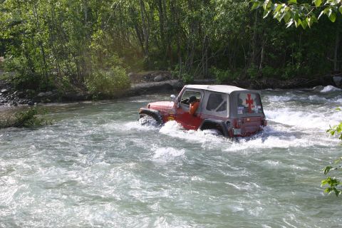 2003 Jeep TJ - A red Jeep Wrangler navigates a rocky riverbed, kicking up spray as it moves through the water.