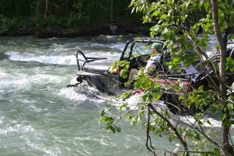 2003 Jeep TJ - A black 2003 Jeep TJ navigates through a fast-moving river, with trees and foliage framing the scene.