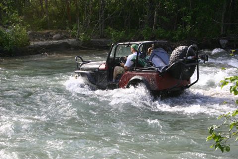 2003 Jeep TJ - A Jeep Wrangler navigates a rocky riverbed, kicking up spray as it goes.