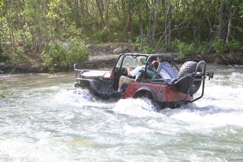 2003 Jeep TJ - A red Jeep Wrangler navigates a shallow river, kicking up spray.