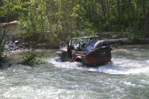 2003 Jeep TJ - A red Jeep Wrangler navigates a shallow river surrounded by trees.