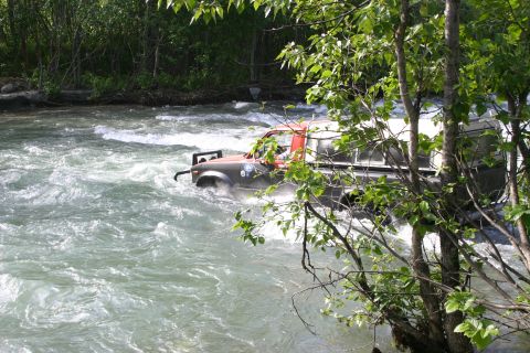 2003 Jeep TJ - An off-road vehicle navigates a turbulent river, with trees and foliage in the foreground.