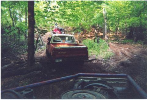 1996 Ford Bronco - Faded red pickup truck navigating a muddy wooded off-road trail in summer.