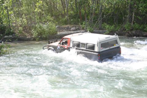 2003 Jeep TJ - A pickup truck navigates a fast-moving river, its tires submerged in the turbulent water.