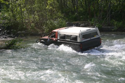 2003 Jeep TJ - Pickup truck navigates a river crossing, kicking up water.