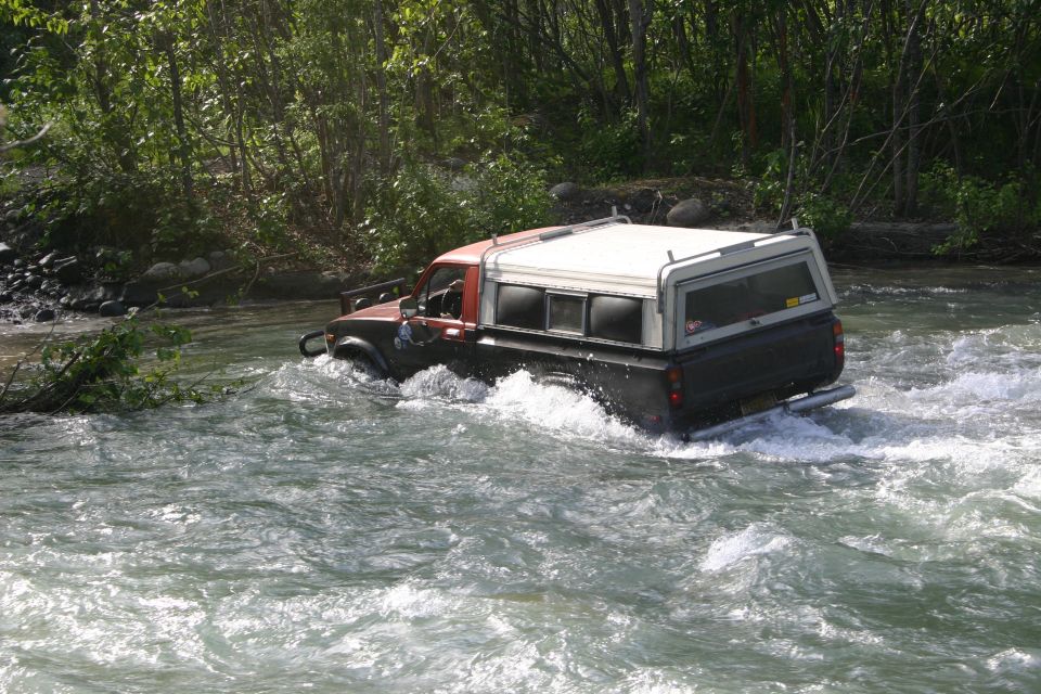 Pickup truck with a camper shell driving through a river with trees in the background