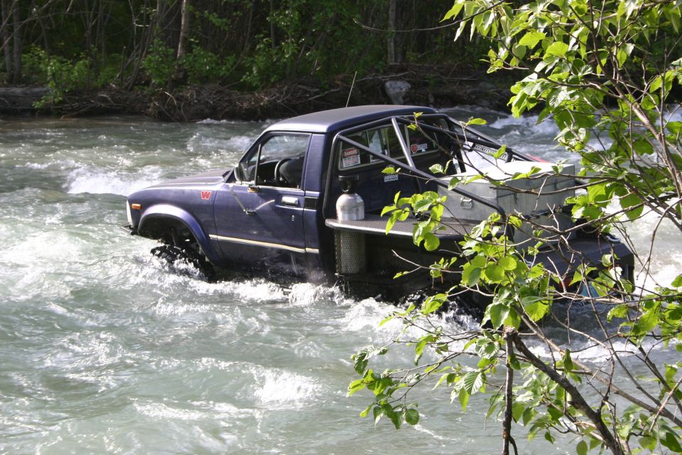 Blue pickup truck navigating a river with a roll cage and storage box