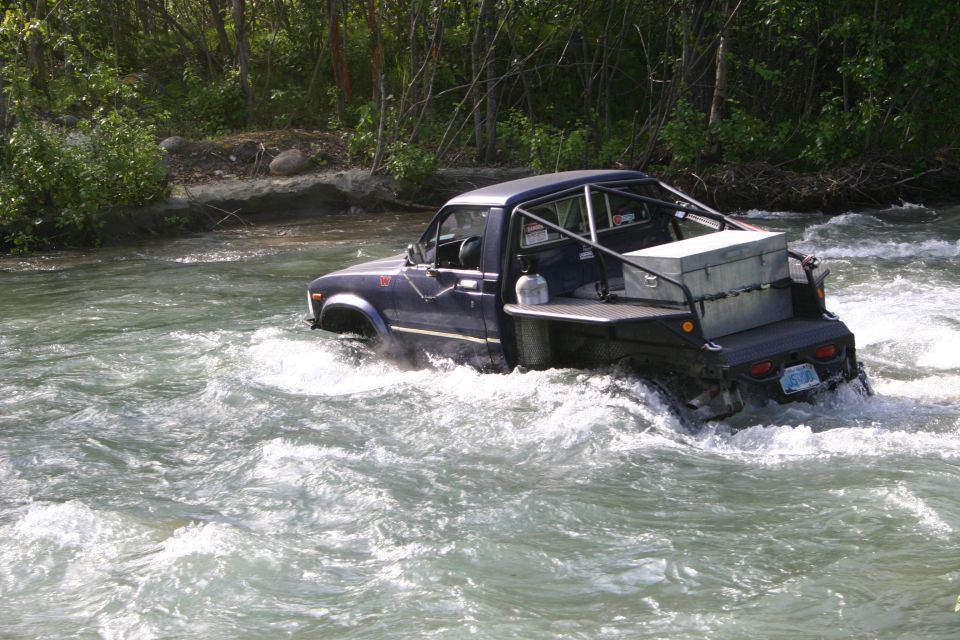 Dark blue Toyota pickup truck with a roll cage and toolbox driving through a river