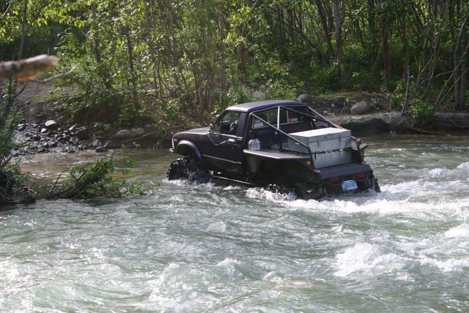 Dark pickup truck with large tires driving through a river