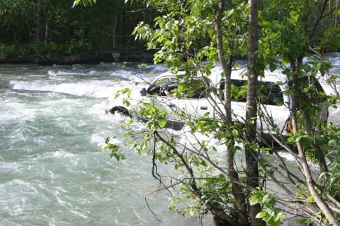 2003 Jeep TJ - A white SUV navigates a turbulent river, with trees in the foreground.