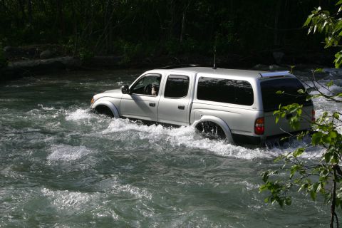 2003 Jeep TJ - Silver pickup truck navigates through a fast-moving river.