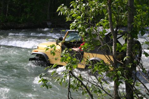 2003 Jeep TJ - A yellow Jeep Wrangler navigates a fast-flowing river, with trees in the foreground.