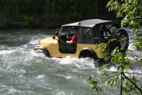 2003 Jeep TJ - Yellow Jeep Wrangler navigates a river, kicking up water.