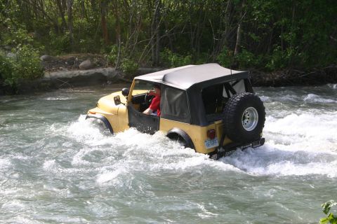 2003 Jeep TJ - A yellow Jeep Wrangler navigates through a flowing river, kicking up water.