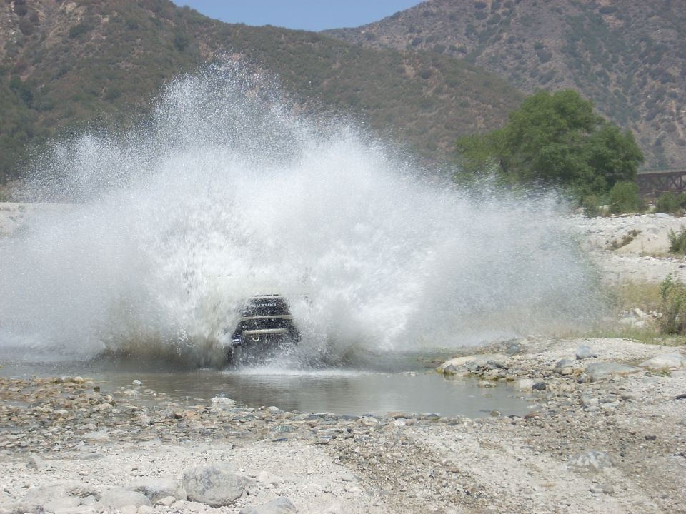 Dark SUV splashing water while crossing a river, rear view