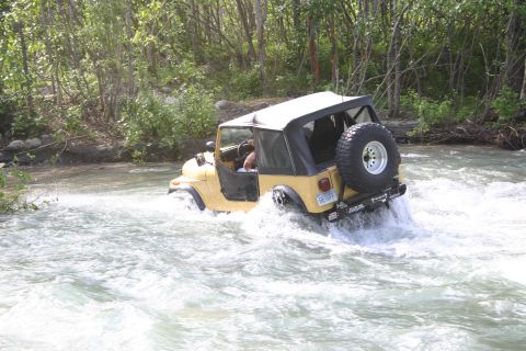 2003 Jeep TJ - A yellow Jeep TJ navigates a rocky riverbed, kicking up spray as it drives through the water.
