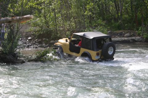 2003 Jeep TJ - Yellow 2003 Jeep TJ navigating a river with trees and rocks in the background.