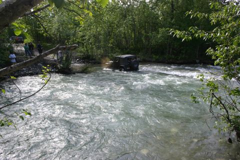 2003 Jeep TJ - A group of off-road vehicles navigates a shallow river during an outdoor excursion.