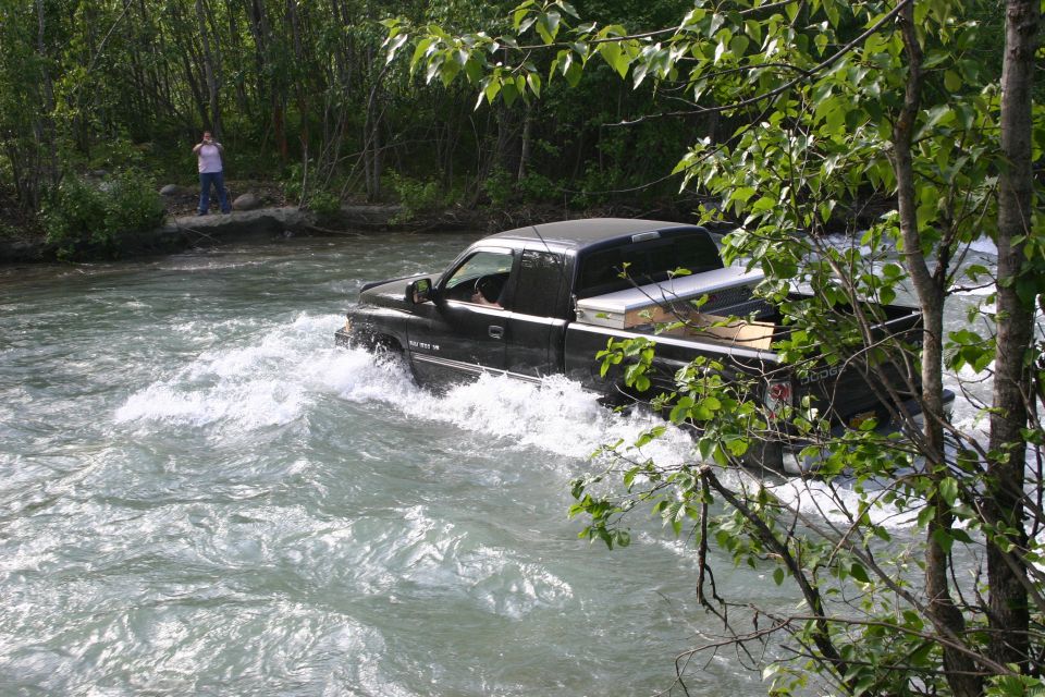 Black pickup truck with a silver toolbox in the bed drives through a fast-moving river
