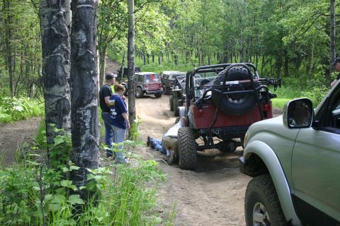 2003 Jeep TJ - A group of Jeeps are on a dirt trail, with one red Jeep Wrangler being worked on from underneath.