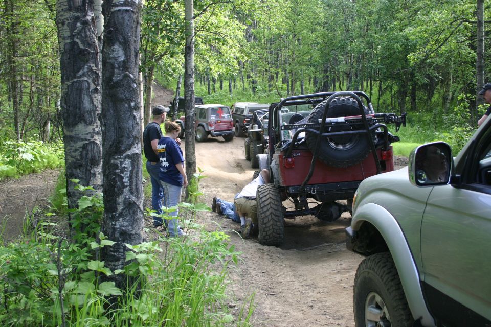 Red Jeep Wrangler rear view with spare tire and roll cage. A person is working underneath