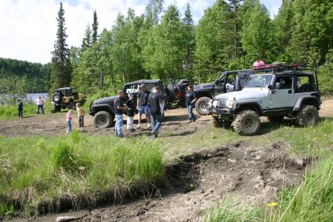 2003 Jeep TJ - Several off-road vehicles are gathered in a wooded area near a lake.