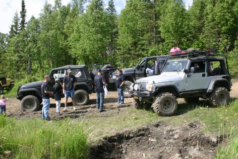2003 Jeep TJ - Several Jeeps, including a silver 2003 TJ Rubicon, are gathered off-road in a wooded area.
