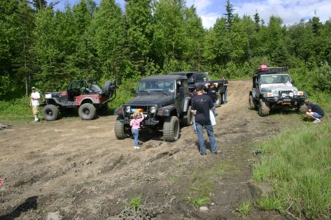 2003 Jeep TJ - A group of Jeeps are gathered on a dirt trail surrounded by trees, with people standing around them.