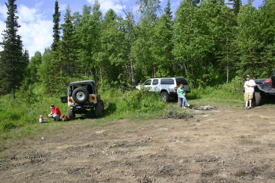 Yellow Jeep Wrangler with spare tire on rear door, parked on dirt road near trees