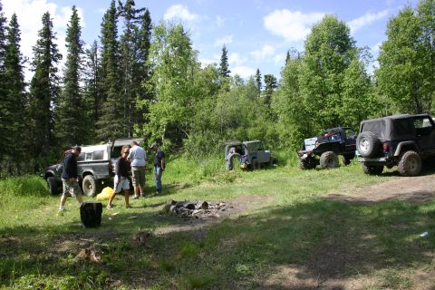 2003 Jeep TJ - Off-road vehicles gathered in a wooded area with a campfire pit in the foreground.